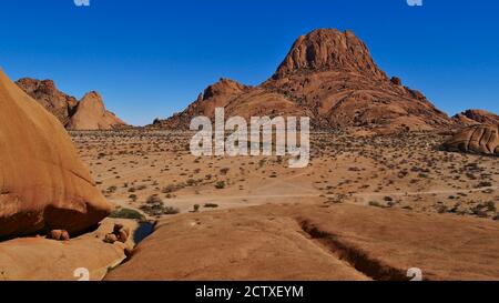 Panoramablick über Spitzkoppe, Kalahari Wüste, Namibia, mit kleinem Wasserteich und runden bräunlichen Felsen an sonnigen Tagen mit blauem Himmel. Stockfoto