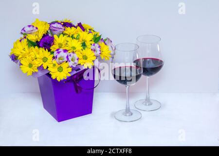 Schöne helle bunte Bouquet mit gelben Chrysantheme und lila eustoma Blumen in einer Schachtel und Rotwein in einem Glas Weißer Hintergrund Stockfoto