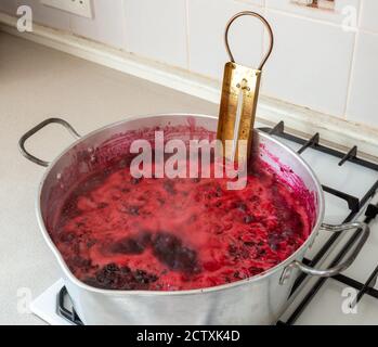 Marmelade machen - ein traditionelles Messingthermometer in einer Konservierung Pfanne mit kochender Brombeere und Apfelmarmelade Stockfoto