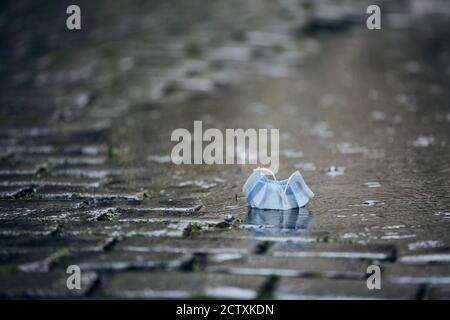 Gebrauchte Einweg-Gesichtsmaske in Pfütze bei Regen. Themen Coronavirus Probleme und das Leben in neuer Normalität. Stockfoto