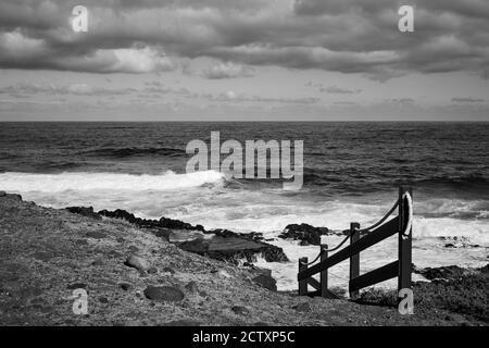 Der Atlantische Ozean und gelenkte Fußweg am Strand auf Teneriffa, Kanarische Inseln, Spanien. Kanarische Landschaft. Schwarzweiß-Fotografie Stockfoto