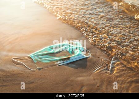 Medizinische Abfälle - Schutzmaske im Wasser an der Strandküste Sand. Meer und Meeresverschmutzung Stockfoto