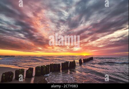 Landschaftlich schöner Sonnenuntergang über dem Meer mit einem alten hölzernen Wellenbrecher. Stockfoto