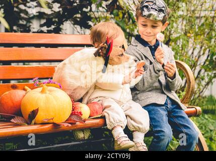 Familie nach Behandlung oder Trick Konzept mit Kindern und Hund Essen Süßigkeiten auf Herbstbank im Garten Stockfoto