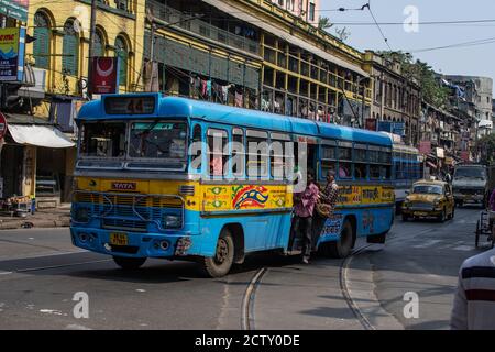 Kolkata, Indien - 2. Februar 2020: Ein blauer und gelber traditioneller öffentlicher Personenbus im Verkehr mit nicht identifizierten Fahrgästen vor einer Straßenbahn Stockfoto