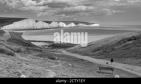 Eineinköpfige Hundewanderin auf dem Seaford Head Pfad mit den Kreidefelsen der Seven Sisters bei Beachy Head im Hintergrund, East Sussex, England Stockfoto