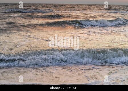 Stürmische weiße Hochglanz Wellen am Meeresstrand in der Nähe Sonnenuntergang Spiegelung in Pastellfarben Stockfoto