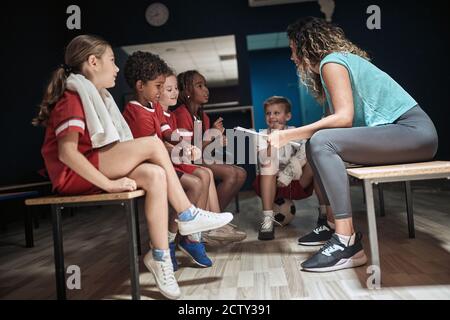 Die Trainerin und ihre kleinen Fußballspieler diskutieren Taktik in Ein Umkleideraum Stockfoto