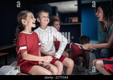 Die Trainerin und ihre kleinen Fußballspieler haben viel Zeit In einem Umkleideraum Stockfoto