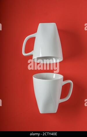 Vertikale Aufnahme von zwei weißen Tassen isoliert auf einem roten Hintergrund Stockfoto
