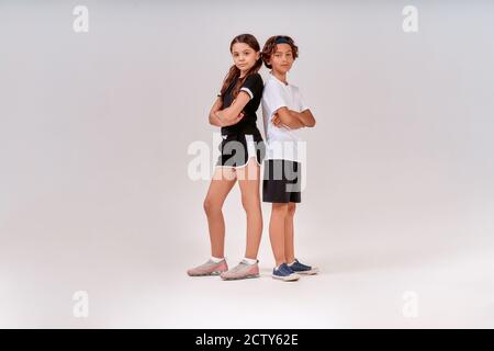 Zwei Teenager, niedlichen Jungen und Mädchen in Sportkleidung Blick auf Kamera, während posiert isoliert über grauen Hintergrund. Kinder, die Sport treiben Stockfoto