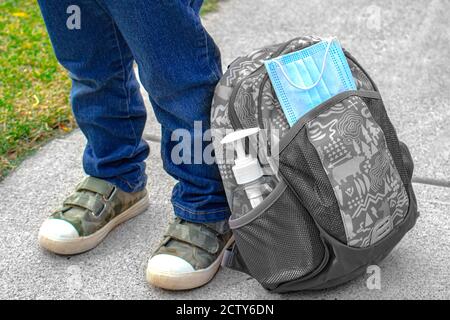 Kinderschuhe neben einer Schultasche mit einem Gesicht Maske und Handdesinfektionsmittel Stockfoto