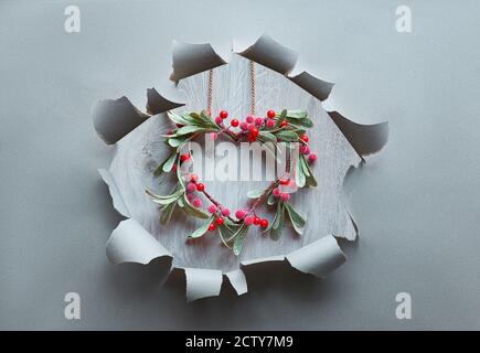 Papierloch mit Weihnachtskranz in Mistelform mit roten Beeren, traditionelle Weihnachtsschmuck. Stockfoto