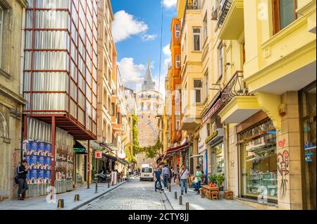 Eine bunte, belebten Straße von Cafés, Geschäften und eine streunende Katze mit der Galata Turm hinter, in Istanbul, Türkei. Stockfoto