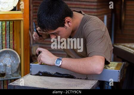 Damaskus ,Syrien 03/27/2010: Nahaufnahme eines jungen Künstlers bei der Arbeit. Er schnitzt sorgfältig eine Kupferplatte mit traditionellen Dekorationen mit Hammer Stockfoto