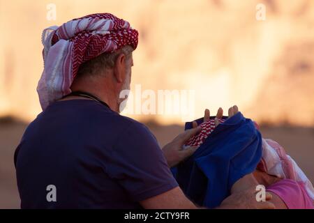 Nahaufnahme eines älteren kaukasischen Paares, das wadi Rum besucht.die Touristen tragen die traditionelle Kopfbewicklung (Keffiyeh). Der Mann hilft seiner Frau Stockfoto