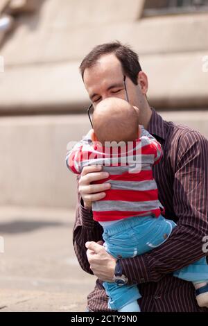Barcelona, Spanien 05/01/2010: Nahaufnahme Porträt eines jungen und glücklichen Vaters mit seinem Baby in den Armen. Das neugierige hübsche Kind greift zu Papa' Stockfoto