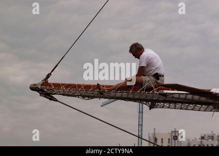 Barcelona, Spanien, 05/01/2010: Ein athletischer Seemann sitzt auf dem hölzernen Bugsprit eines großen Schiffes, das versucht, es zu reparieren. Er trägt kein schützendes e Stockfoto