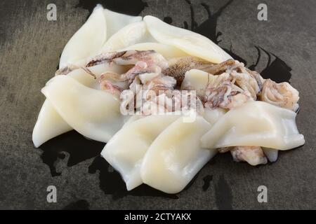 Nahaufnahme von rohen Tintenfischröhrchen und Tentakeln auf verwittertem Schwarz Schneidebrett Stockfoto
