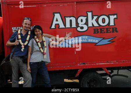 Der niederländische Abenteuerfotograf Hans Kemp und seine thailändische Freundin Lah tragen traditionelle kambodschanische Jasminkränze vor einem Angkor Beer Truck. Phnom Penh Kambodscha. © Kraig Lieb Stockfoto