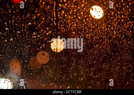 Regentropfen auf dem Glas des Autos, beleuchtet von Straßenlampen in der Nacht. Stockfoto