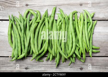 Viele grüne Bohnenschoten auf alter Holzbank. Wunderschöne Draufsicht Anordnung der hausgewachsenen blauen See Pole Bean Ernte. Konzept für autarken Garten Stockfoto