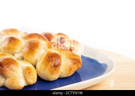 Mehrere kleine geflochtene Brötchen. Weißes Hefebrot mit Eierwäsche auf blauem und weißem Teller. Perspektivische Ansicht. Authentische Schweizer Butterbrot Rezept genannt ZOP Stockfoto