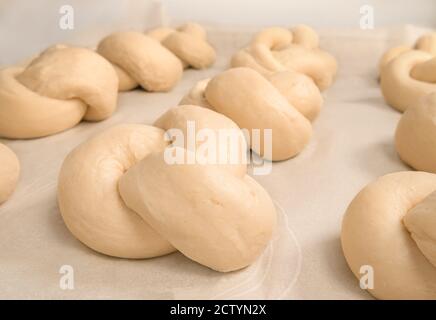 Hausgemachte Hefegebäck in einem Knoten gebunden. Traditionelle Schweizer Brot Rezept genannt Zopf oder Butterzopf. Die Teigknoten sind in Reihen auf Backpapier angeordnet, Stockfoto