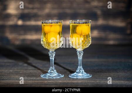 Hausgemachte Tinktur von gelben Kirsche Pflaume in einem zwei-Wein-Kristallglas auf Holzhintergrund, Ukraine, Nahaufnahme. Berry alkoholische Getränke Konzept Stockfoto