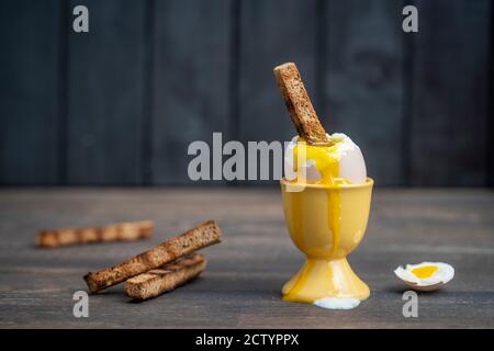 Weich gekochtes braunes Ei und Toast Brot in Eierbecher auf Holztisch Hintergrund. Nahaufnahme. Gesundes Frühstück Stockfoto