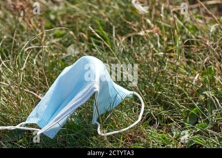 Gebrauchte blaue Gesichtsmaske auf dem Boden im Gras. Gesichtsmaske ist falsch entsorgt. Umweltverschmutzung und Umweltkatastrophe. Covid-19 Pandemie Stockfoto