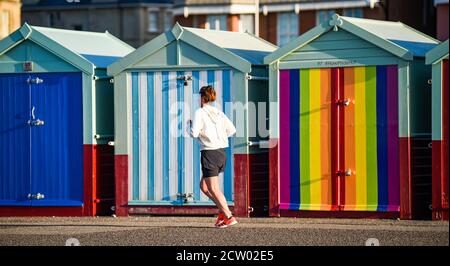 Brighton, Großbritannien. September 2020. Ein Läufer passiert bunte Strandhütten entlang der Küste von Hove an einem hellen und sonnigen, aber kalten Morgen an der Südküste. : Credit: Simon Dack/Alamy Live News Stockfoto