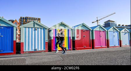 Brighton, Großbritannien. September 2020. Läufer kommen an bunten Strandhütten entlang der Küste von Hove an einem hellen und sonnigen, aber kalten Morgen an der Südküste vorbei. : Credit: Simon Dack/Alamy Live News Stockfoto