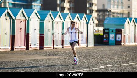 Brighton, Großbritannien. September 2020. Ein Läufer passiert bunte Strandhütten entlang der Küste von Hove an einem hellen und sonnigen, aber kalten Morgen entlang der Südküste. : Credit: Simon Dack/Alamy Live News Stockfoto