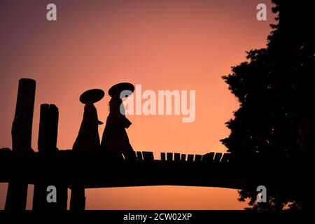 Silhouette von zwei buddhistischen Mönchen, die bei Sonnenuntergang auf der U Bein Brücke in Amarapura, Myanmar, wandern Stockfoto