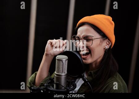 Porträt einer fröhlichen jungen Frau, Hip-Hop-Künstler suchen konzentriert, singen in einem Kondensator Mikrofon, während die Aufnahme eines Songs in einem professionellen Studio Stockfoto