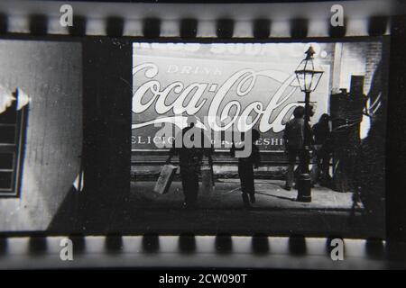 Feine Vintage-Schwarz-Weiß-Fotografie der 1970er Jahre von Profilen von Stadtmenschen, die vor einer riesigen Coca-Cola-Anzeige auf einer Wand gemalt gehen. Stockfoto