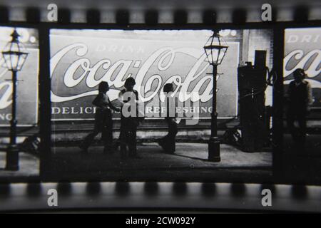 Feine Vintage-Schwarz-Weiß-Fotografie der 1970er Jahre von Profilen von Stadtmenschen, die vor einer riesigen Coca-Cola-Anzeige auf einer Wand gemalt gehen. Stockfoto