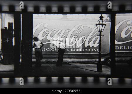 Feine Vintage-Schwarz-Weiß-Fotografie der 1970er Jahre von Profilen von Stadtmenschen, die vor einer riesigen Coca-Cola-Anzeige auf einer Wand gemalt gehen. Stockfoto