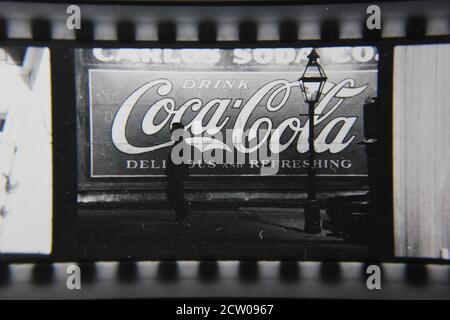 Feine Vintage-Schwarz-Weiß-Fotografie der 1970er Jahre von Profilen von Stadtmenschen, die vor einer riesigen Coca-Cola-Anzeige auf einer Wand gemalt gehen. Stockfoto