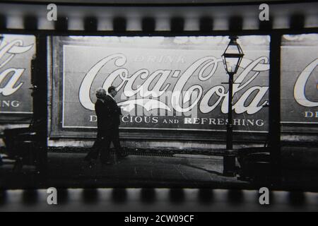 Feine Vintage-Schwarz-Weiß-Fotografie der 1970er Jahre von Profilen von Stadtmenschen, die vor einer riesigen Coca-Cola-Anzeige auf einer Wand gemalt gehen. Stockfoto