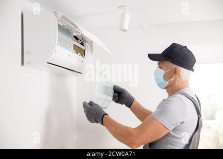 Reinigung der Klimaanlage. Arbeiter in Handschuhen und medizinische Maske überprüft Filter Stockfoto