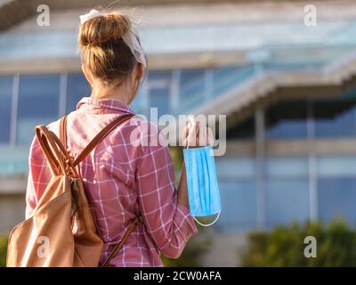 Junge Studentin mit Rucksack und Gesichtsmaske vor der Universität. Speicherplatz kopieren. Stockfoto
