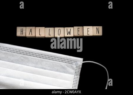 Halloween dunkelschwarzer Hintergrund mit Holzwürfeln geschriebenem Halloween und einer Sicherheitsmaske für Coronavirus, Covid-19 und Halloween Konzept Stockfoto