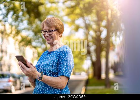 Glückliche ältere Frau mit Handy im Freien Stockfoto