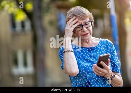 Gestresste ältere Frau mit Handy im Freien Stockfoto