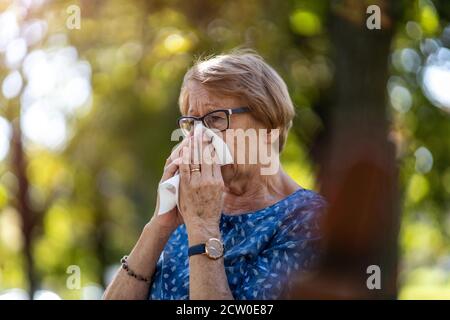 Ältere Frau bläst ihre Nase draußen Stockfoto