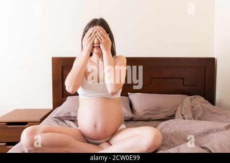 Junge hübsche schwangere Frau mit Kopfschmerzen zu Hause im Bett. Stockfoto