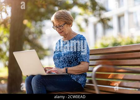 Ältere Frau mit Laptop auf der Bank im Freien Stockfoto