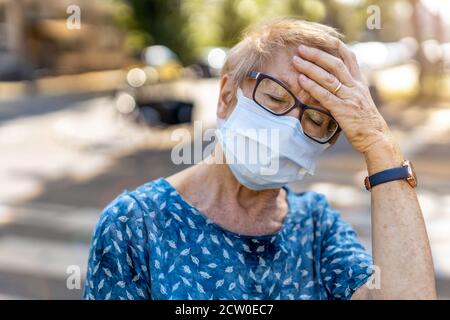 Ältere Frau mit schützender Gesichtsmaske, die an Kopfschmerzen leidet Stockfoto